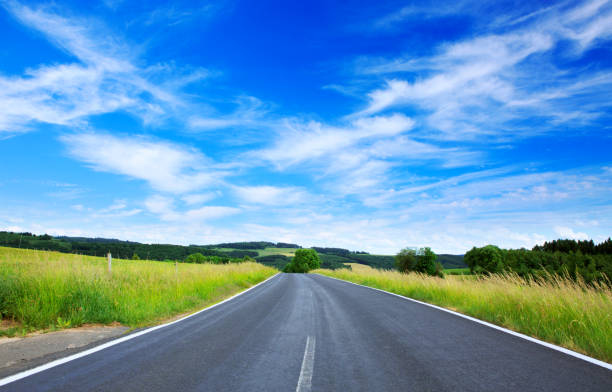 istock Asphalt road through the green field and clouds on blue sky 944519398