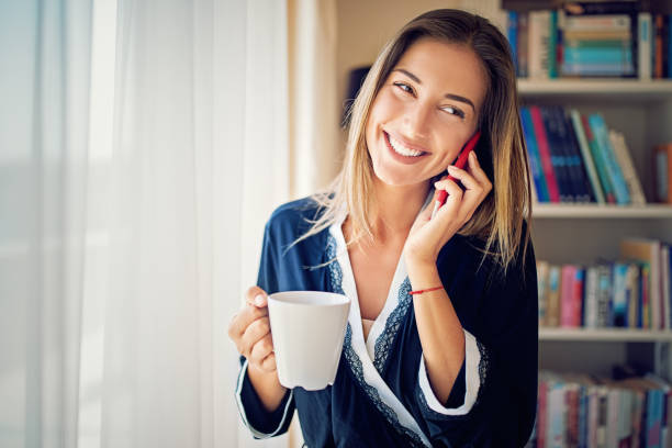 jeune femme boit du café le matin et parler à l’aide de son téléphone portable - joy the human body smiling women photos et images de collection