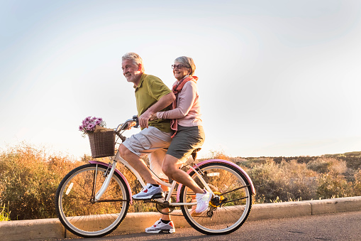 two senior man and woman together on  an old bicycle outdoor activity. Happiness and freedom from work concept. sunlight and smiles.