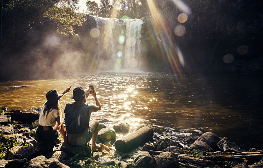 Shot of a young couple taking photos of a waterfall over a lake