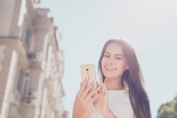 istock Smiling woman reading message on  mobile phone while standing on  the street 944543738