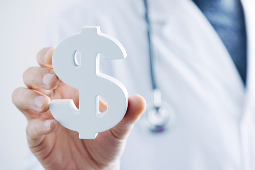 closeup of a young caucasian doctor man with a dollar symbol in his hand, depicting the concepts of the healthcare industry or the healthcare costs