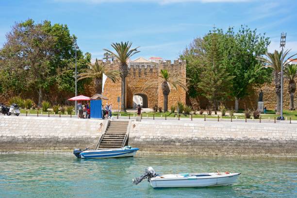 View of the entrance arch of the Governors Castle (Castelo dos Governadores) with small boats moored in the foreground and tourists enjoying the setting, Lagos, Algarve, Portugal, Europe.