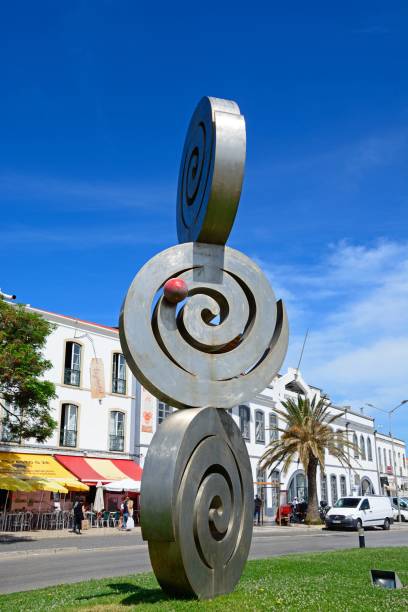 Modern art coiled disk sculpture along Avenida dos Descobrimentos with people going about their business, Lagos, Algarve, Portugal, Europe.
