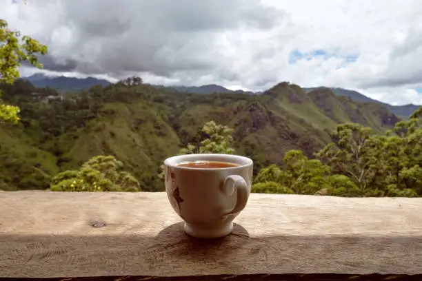 Photo of A glass of hot tea on table in tea shop and view on Small dams Peak in Sri Lanka.