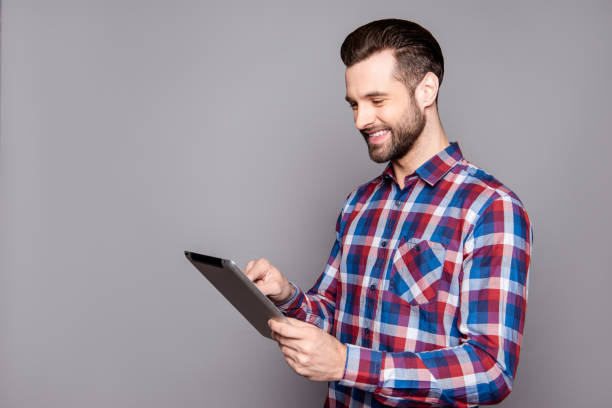 istock Smiling stylish man isolated on gray background holding his tablet and reading information 944562024