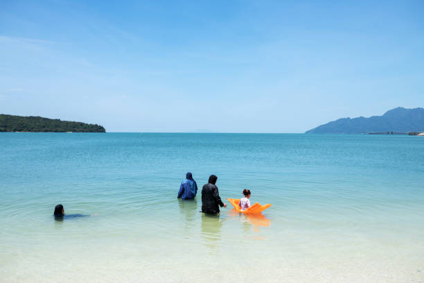Langkawi, Malaysia - February 28, 2018 : Four female Muslims in the water on the beautiful Cenang beach.