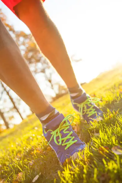 Image of human legs in sportshoes running down green spring grass.