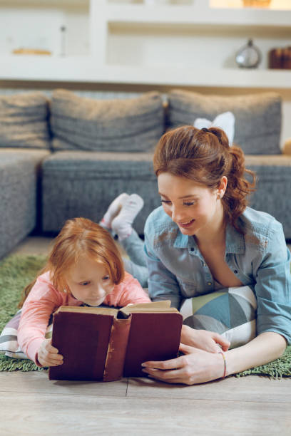 istock Mother reading a book to her daughter on carpet 944573828