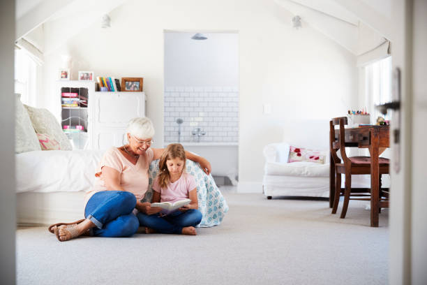 grand-mère et petite-fille de lire un livre dans sa chambre - grandparent family reading inside of photos et images de collection