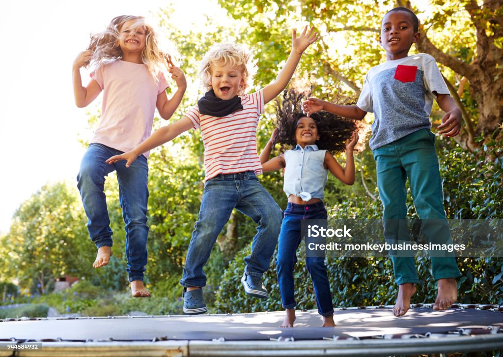 Four kids having fun together on a trampoline in the garden Child Stock Photo