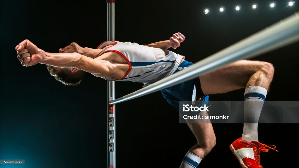 Male high jumper clearing bar Male high jumper jumping over the bar against black background. Jumping Stock Photo