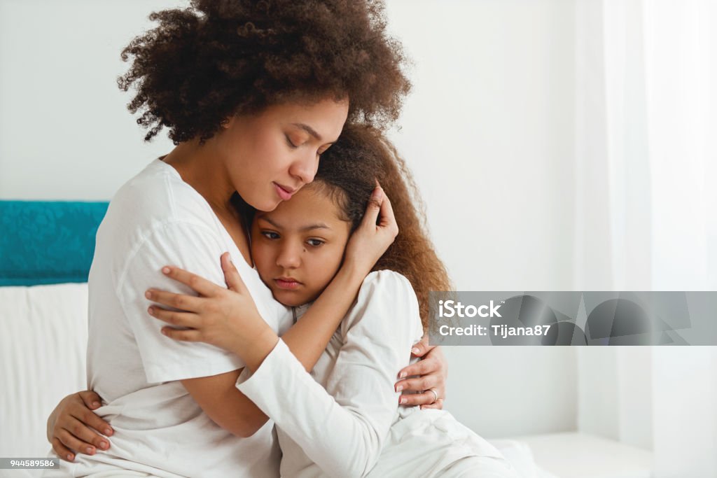 Madre consuela a su hija, sentada en el dormitorio, abrazos - Foto de stock de Niño libre de derechos