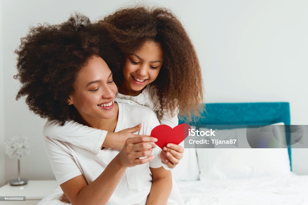 Mother and daughter enjoying on the bed, holding a heart Mother Stock Photo