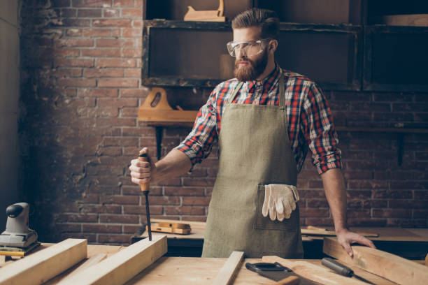istock concenrated handsome cabinetmaker with chisel think. Stylish craftsman with brutal hairstyle and glasses 944605346