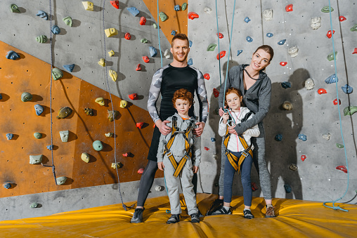 Family with children standing together near climbing walls at gym and looking at camera
