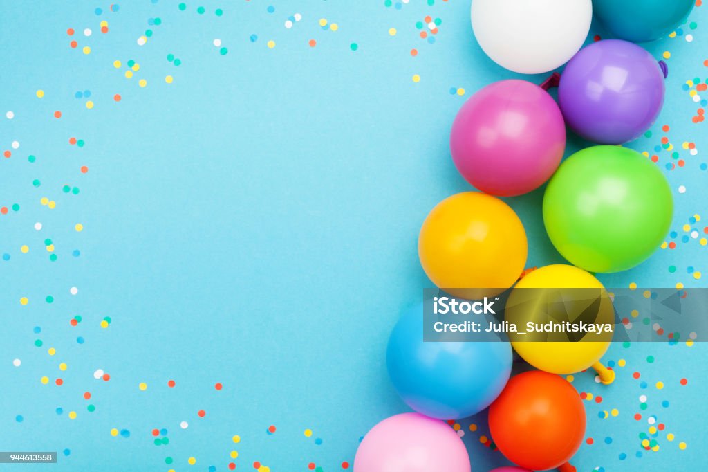 Confetti and colorful balloons for birthday party on blue table top view. Flat lay style. Confetti and colorful balloons for birthday party on blue table top view. Flat lay style. Frame for greeting text. Birthday Stock Photo