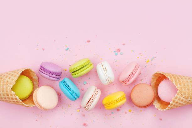 istock Waffle cone with colorful macaron or macaroon on pink background top view. Flat lay composition. 944613590