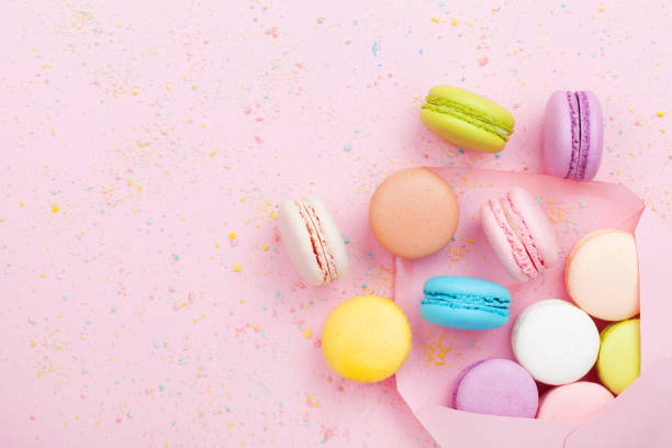 istock Creative composition with envelope and cake macaron or macaroon on pink pastel confetti background top view. 944613788