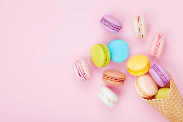 istock Waffle cone with colorful macaron or macaroon on pink pastel background top view. Flat lay. 944613848