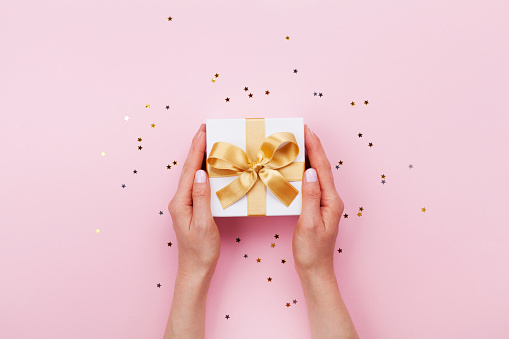 Mujer manos con regalo o presente caja decoración confetti en vista rosa pastel mesa. Cumpleaños o boda plantilla o maqueta. photo