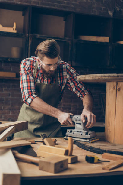 istock serious handsome  craftsman work with sander for wood. Stylish young cabinet-maker with brutal hairstyle and saved glasses work at his workstation. He love his job 944614512