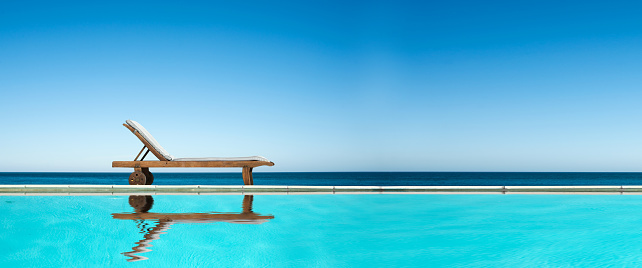 Reclining chair near a swimming pool, sea and blue sky panoramic background