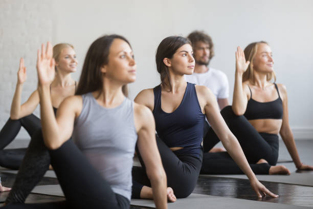 istock Group of young sporty people in Matsyendrasana pose, close up 944619752