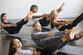 Group of young sporty people in Paripurna Navasana pose