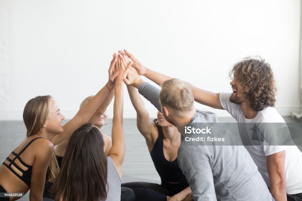 Group of fit happy people giving high five Group of fit happy people giving high five in fitness studio room, celebrating success. Setting goals, achieving team result. Teamwork, unity, support, motivation, active healthy life benefits concept Celebration Stock Photo