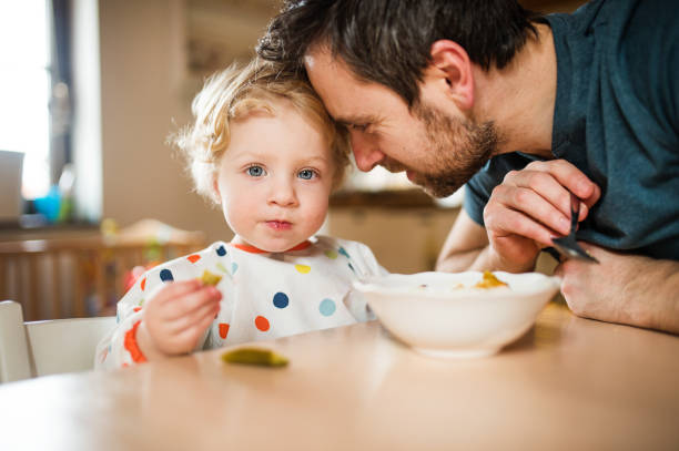 padre alimentando a un niño pequeño en casa. - domestic kitchen father eating child fotografías e imágenes de stock