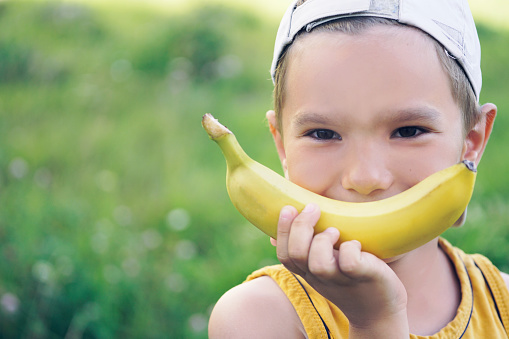 Face of a beautiful young boy in cap with banana smile on nature background.