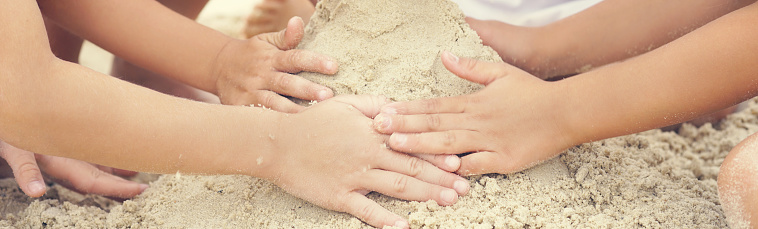 Group of children build a sand tower, hands closeup.