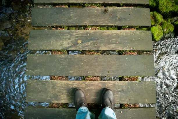 Looking down at your feet on a wooden bridge over a small river