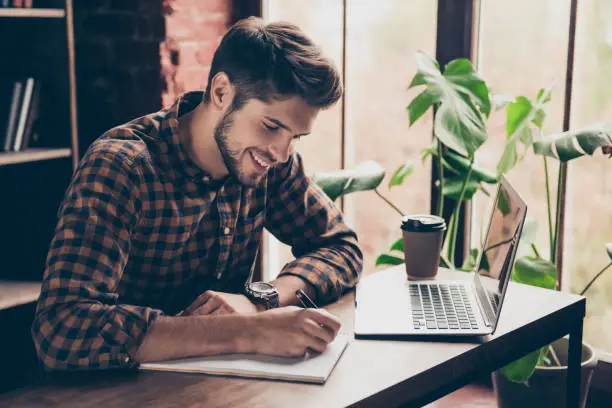 Photo of Smiling handsome student working with laptop and making notes