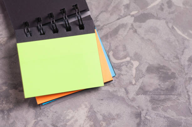 istock Opened notebook with spiral and blank rectangle pages green orange and blue color on old concrete gray cement with copy space 944655360