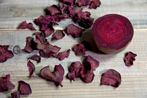 January, 14th, 2015: Cross section of a fresh beet and chopped dried crunchy beet chips on wooden cutting board