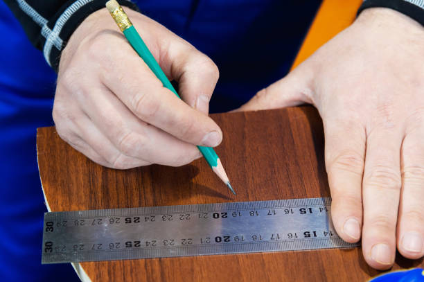 istock Close-up Men's hands draw a pencil on the ruler with a sub-standard template for cutting out furniture details next to the jigsaw and furniture clips 944667536