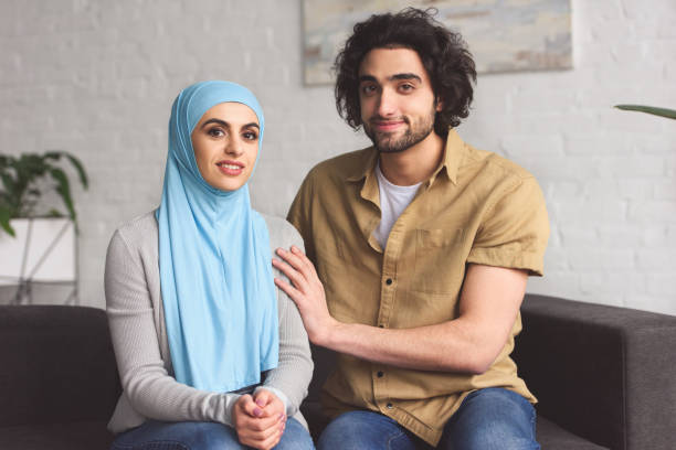 istock muslim couple sitting on sofa and looking at camera at home 944667926