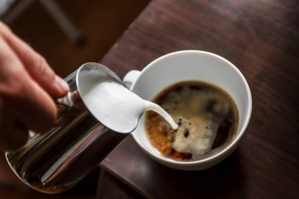 man pouring into a cup of coffee with milk stock photo