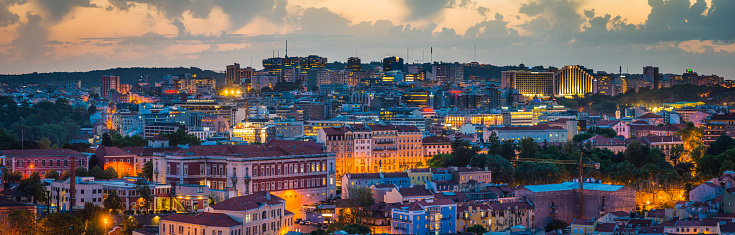 Panoramic view across parkland and dusty roads, apartment buildings and highrise offices along the illuminated city skyline of Lisbon, Portugal at night.