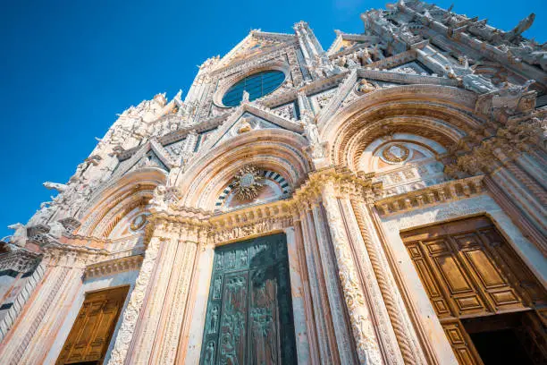 Wide angle image showing the Intricately carved marble and ornate entrance doors on the ancient facade of Siena Cathedral in Tuscany, Italy.