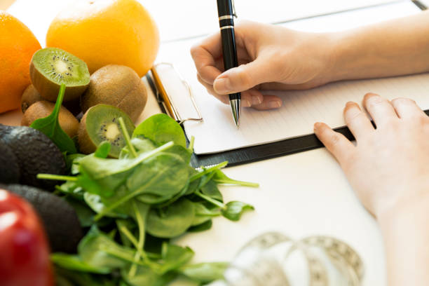 nutritionist woman writing diet plan on table full of fruits and vegetables - health plan imagens e fotografias de stock