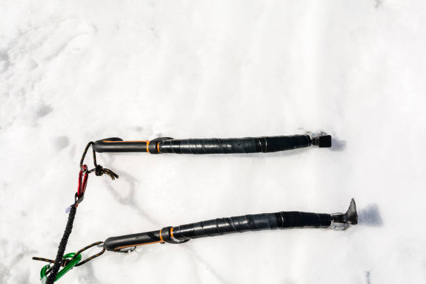 Two ice axes stuck in the snow with carabiners and lanyards. Used for winter and ice climbing.