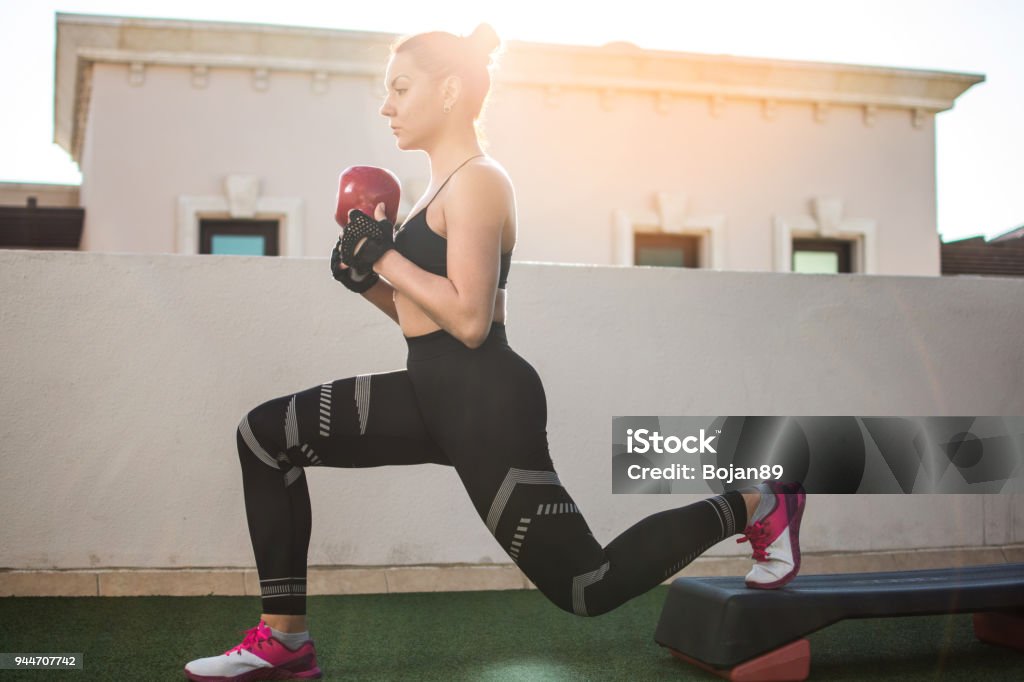 Fit sportswoman exercising with kettle bell on fitness stepper outdoors. Lunge Stock Photo