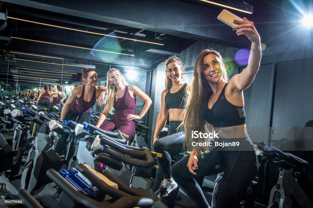 Sporty girls taking selfie while sitting on exercise bikes in gym Gym Stock Photo