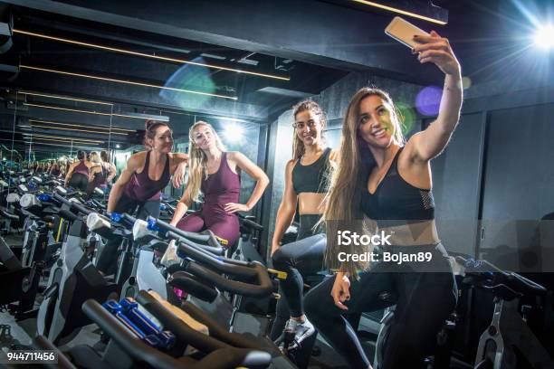 Sporty Girls Taking Selfie While Sitting On Exercise Bikes In Gym Stock Photo - Download Image Now