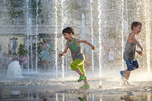 szczęśliwe dzieci bawią się grając w fontannie miejskiej w upalny letni dzień. - fountain zdjęcia i obrazy z banku zdjęć