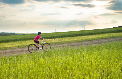 Sporty girl with bicycle in green field, summer rural landscape