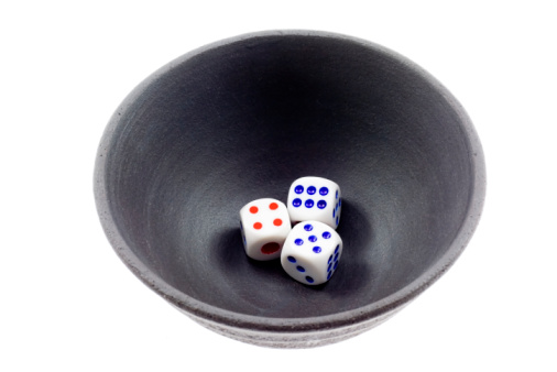 Close up of black cup tumbler mug with green felt cover and five white dice rolling out of it showing different numbers on white background as concept for dice poker and gambling